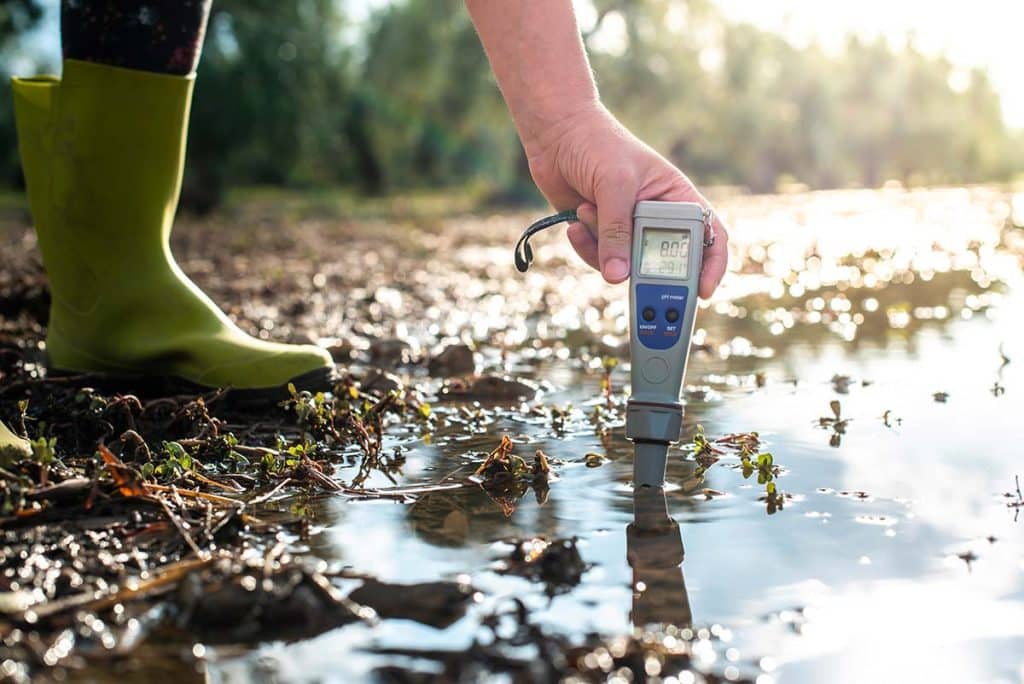 A researcher kneels in a field recording data beside sampling tools. Biochar can be evaluated in controlled trials to measure impacts on soil structure, nutrient retention, and water movement.